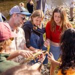A professor points at a fish he is holding while students gather around attentively