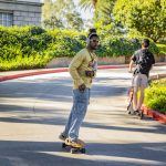 Young man wearing headphones is riding a skateboard down the hill in front of Hall of Letters on the University of Redlands campus.