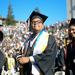 Proud-looking male student in graduation cap and gown. Numerous ribbons and stoles are draped over his shoulders. 